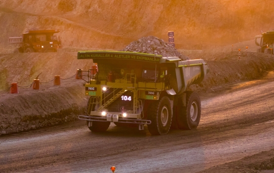 Two heavy haul trucks driving up a road at sunset