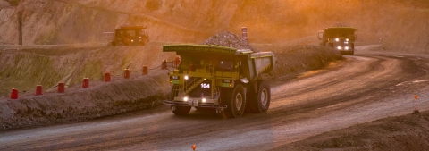 Two heavy haul trucks driving up a road at sunset